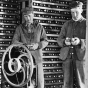 Black and white photograph of Martin Carlsted turning the handle of a manual corn sheller to remove kernels, c.1910.