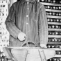 Black and white photograph of Martin Carlsted turning the handle of a manual corn grader to grade and separate different sizes and shapes of kernels, c.1910.