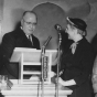 Black and white photograph of Minnesota Supreme Court Justice Roger L. Dell presenting Crookston BPW member Mae Rideout with a “book of golden deeds” in St. Paul, April 12, 1954. 