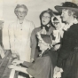 Black and white photograph of BPW members in historic costumes singing around a piano, 1958. Pictured (left to right) are Louise Rasmussen, Clara Berg, Ruth Rohrer (piano player), an unknown woman, and Maybelle Anderson.