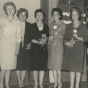 Black and white photograph of Mrs. Matzke, Miss Olson, and Miss Nelson present yellow carnations to initiates Luverne Sorenson, Deborah Hanson, Eloise Espe, and Clara Kelly at an initiation meeting for new BPWC members, 1966.