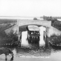 photograph of small steamboat passing under a bridge