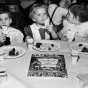 Black and white photograph of three children attending a Passover seder at the St. Paul Talmud Torah, 1960. The children are Susan Hoffman, Lisa Savitt, and Scott Zuckman.