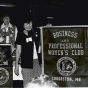 Black and white photograph of Crookston BPW president Betty Brecto watches as BPWC members Eleanor Johnson and Norma Van Horn, two BPW members, reveal the new Crookston BPWC banner on March 11, 1977.