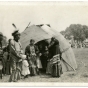 An Ojibwe family standing by bull rush wigwam