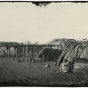 Black and white photograph of a Ho-Chunk woman sitting outside a shelter. Taken by Benjamin Franklin Upton in 1858.