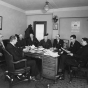 photograph of a group of men gathered around a desk in the State Office Building