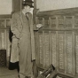 Black and white photograph of Richard R. Sackett, in charge of a historical records survey crew salvaging old documents at the second state capitol prior to demolition, inspects oak paneling, 1937. Photographed by the Minneapolis Tribune.