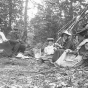 Black and white photograph of Frances Densmore seated on ground with others at Pigeon River, c. 1905.