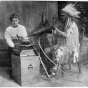 Black and white photograph of Frances Densmore with Mountain Chief who is interpreting a recording. 