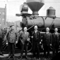 Black and white photograph of the first locomotive to bring iron ore to the Duluth docks with dignitaries and crew members, 1934. 