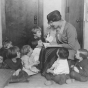 Black and white photograph of a woman reading to children at the Neighborhood House, c.1925.