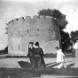 Black and white photograph of women with parasols by round tower, c.1900.