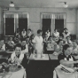 Black and white photograph of Retta Bede with students during a home-cooking class, 1930s.