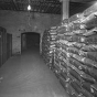 Black and white photograph of sacks of sugar produced by the American Crystal Sugar Company sit in a storage warehouse. Photographed by Norton & Peel on November 30, 1949