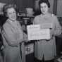 Black and white photograph of two members of the Mount Sinai Women's Auxiliary posing in the Mount Sinai Hospital gift shop holding a sign advertising greeting cards, c.1954.
