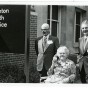 Ruth Boynton with colleagues Don Cowan and Paul Rupprecht at the ceremony where the University Health Service was renamed the Boynton Health Service. She is elderly and sitting in a wheelchair. The two men stand behind her and the sign with the name of the building is in the foreground.