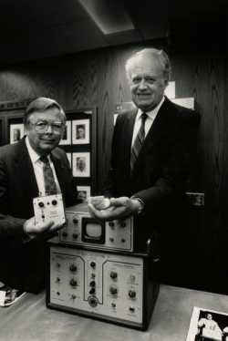 Black and white photograph of Medtronic Founder Earl Bakken and Medtronic CEO Winston Wallin with an early pacemaker model, 1986. Photographed by Jeffrey Grosscup.  