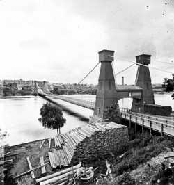 Black and white photograph of the Hennepin Bridge from Nicollet Island, c.1868.