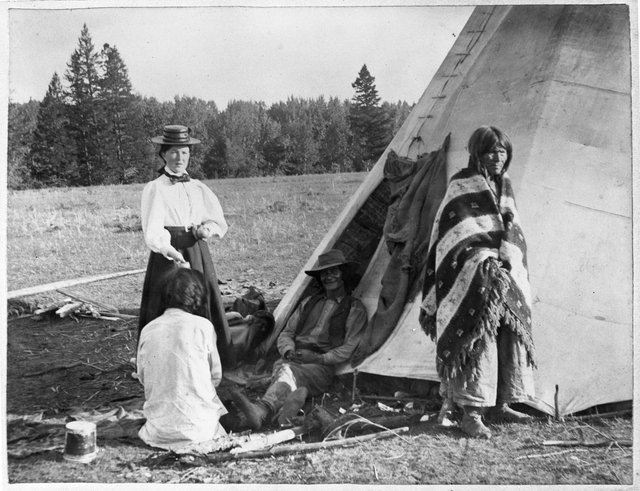 Black and white photograph of Frances Densmore outside of tipi with American Indians, 1900. 