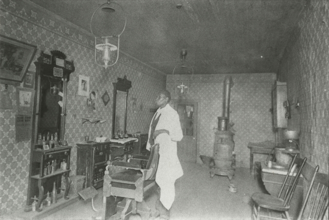 Black and white photograph of African American barber Prince Honeycutt in his Fergus Falls shop, c.1900.