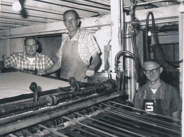 Black and white photograph of staff of the Waconia Patriot at a printing press. Art Wessele is shown in the middle. Date and photographer unknown.