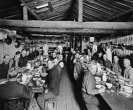 Black and white photograph of Lumberjacks eating in lumber camp dining hall, ca. 1916. 