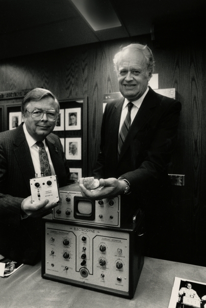 Black and white photograph of Medtronic Founder Earl Bakken and Medtronic CEO Winston Wallin with an early pacemaker model, 1986. Photographed by Jeffrey Grosscup.  