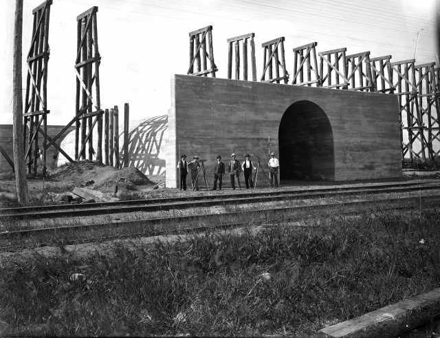 Black and white photograph of Northern Pacific Railway engineers in front of completed concrete archway. View to southwest, fall 1906.