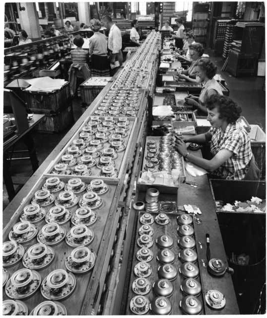Black and white photograph of Honeywell Round thermostats ready for final checkout and packaging at a factory in Golden Valley, c.1955. 