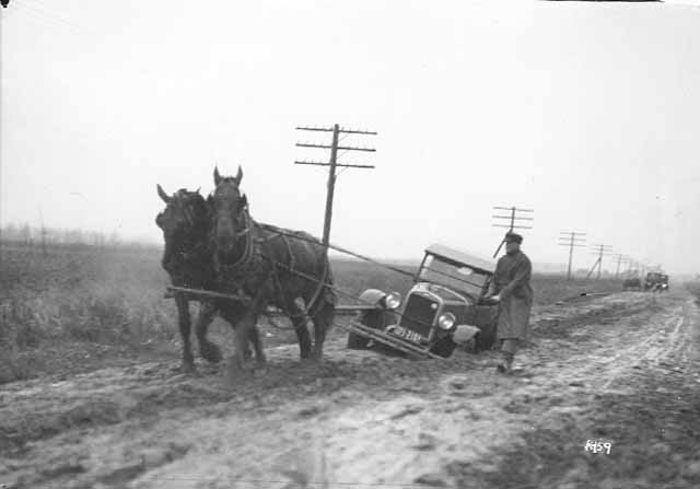 Horses pulling a car out of mud on a dirt road