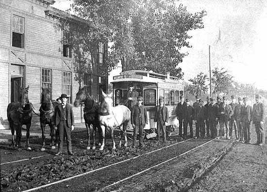 Black and white photograph of a horse-drawn streetcar in Minneapolis; sign reads Sixth Street, Monroe Street and Eighth Avenue, c.1885. This photograph shows a second team of horses ready to relieve the team on the horsecar.