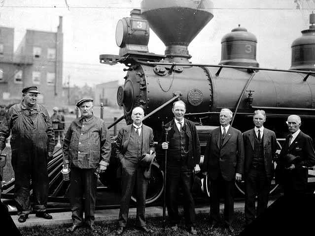Black and white photograph of the first locomotive to bring iron ore to the Duluth docks with dignitaries and crew members, 1934. 