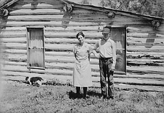Black and white photograph of Mrs. Cornelius and son standing by their log house, homesteaded in 1912.