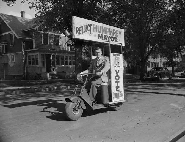 Black and white photograph of a “Hubert Humphrey for mayor” campaign worker rides his Cushman scooter before the Minneapolis mayoral election, 1947. 