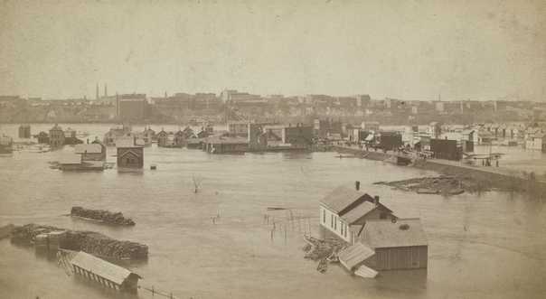 Black and white photograph looking north across the Flats during high water 1881. The raised street is Wabasha.