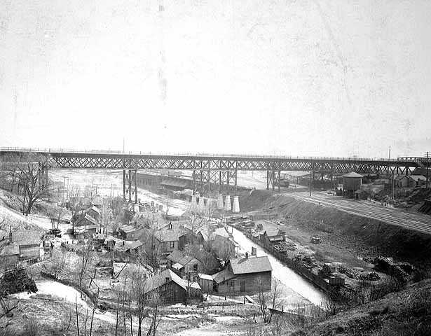 Black and white photograph of Swede Hollow with the Sixth Street Bridge in the background, c.1900.