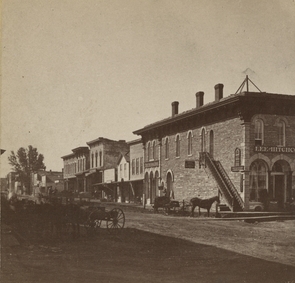 Black and white photograph of Division Street, Northfield 1870. The First National Bank is the first door to the left of the staircase. Photographed by Sumner’s Gallery.  