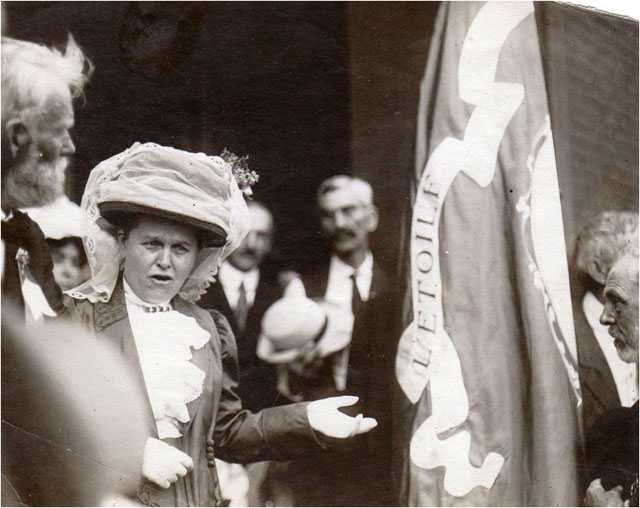 Black and white photograph of Mary Mehegan Hill speaking at a St. Paul event marking the fiftieth anniversary of the First Minnesota Volunteer Infantry Regiment’s departure for Civil War duty, 1911.. Hill presented a duplicate of an old Regimental flag to the group. 