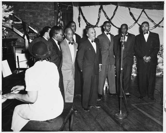 The Wheatley Aires, a men’s singing group, sing in front of an audience at Phyllis Wheatley Community Center (809 Aldrich Avenue North) with a pianist accompanying. ca. 1950.