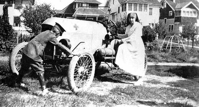 Black and white photograph of a Red Cross nurse, and likely Motor Corps officer, 1918. The car has the Red Cross symbol on the hood and was likely part of the Minnesota Motor Corps. 