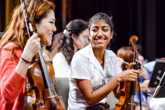 Color image of First Associate Concertmaster Susie Park playing next to a young Cuban violinist in a Side by Side rehearsal. 2015.
