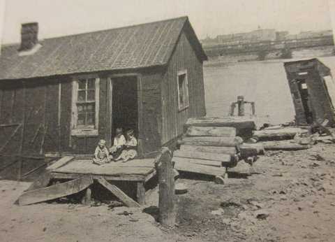 Black and white photograph of a shack and outhouse, river’s edge, 1917