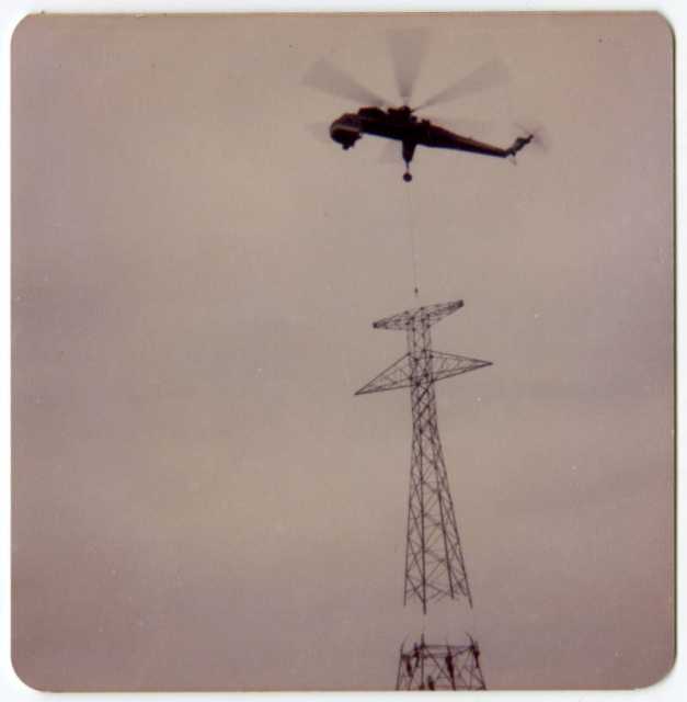 A crane helicopter lining up a power-line tower’s top portion with its base during construction of a high-voltage power line through Grant County, Minnesota, 1976-1978.