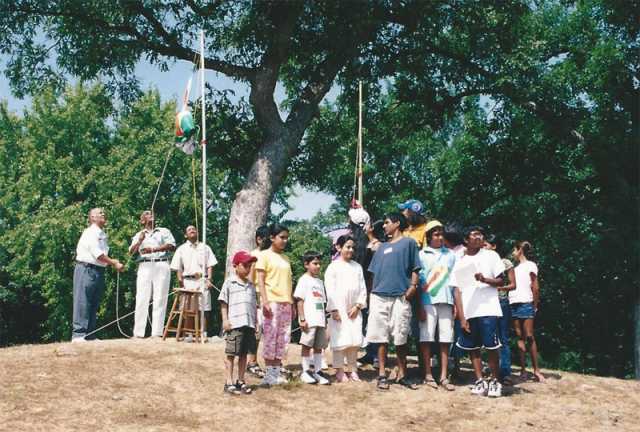 Color image of picnic attendees in St. Paul raise the national flag of India at an event held to celebrate India’s independence from Great Britain. Photographed by Anoop Mathur in August 2003.