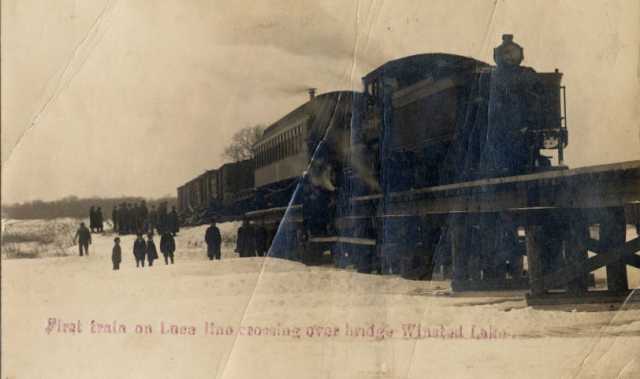 Black and white photograph of the first train on the Luce Line railroad crossing over the bridge at Winsted Lake, ca. 1900.