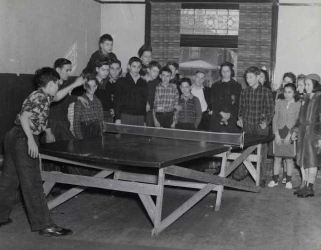 Black and white photograph of two boys playing ping pong at the Jewish Educational Center Annex while a group of children looks on, 1940.
