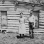 Black and white photograph of Mrs. Cornelius and son standing by their log house, homesteaded in 1912.