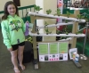 Color image of 4-H club member Alyssa Schwede at the West Polk County Fair with her hydroponic vegetable garden exhibit, 2015. The exhibit was awarded a purple ribbon.