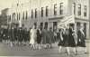 Black and white photograph of Members of Crookston’s BPW club walking with the American flag down Main Street in a parade, ca. 1940s.